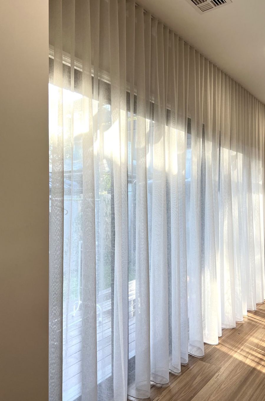 White wave fold sheer curtains along a wall of windows with timber floors